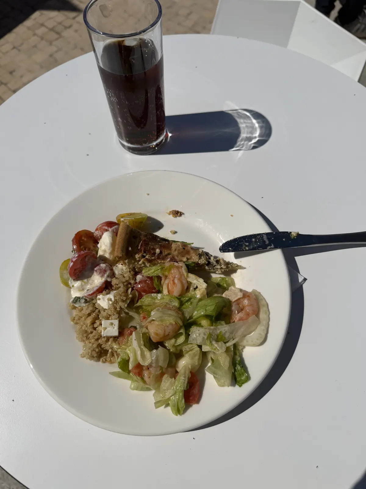 Plate of salad with chickpeas, tomato and cheese on a white table, next to a glass of soda.