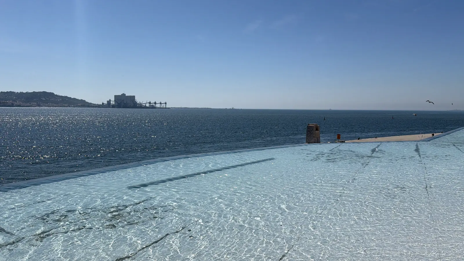 Shallow reflecting pool in the foreground that seems to run into the river, under a clear sky.