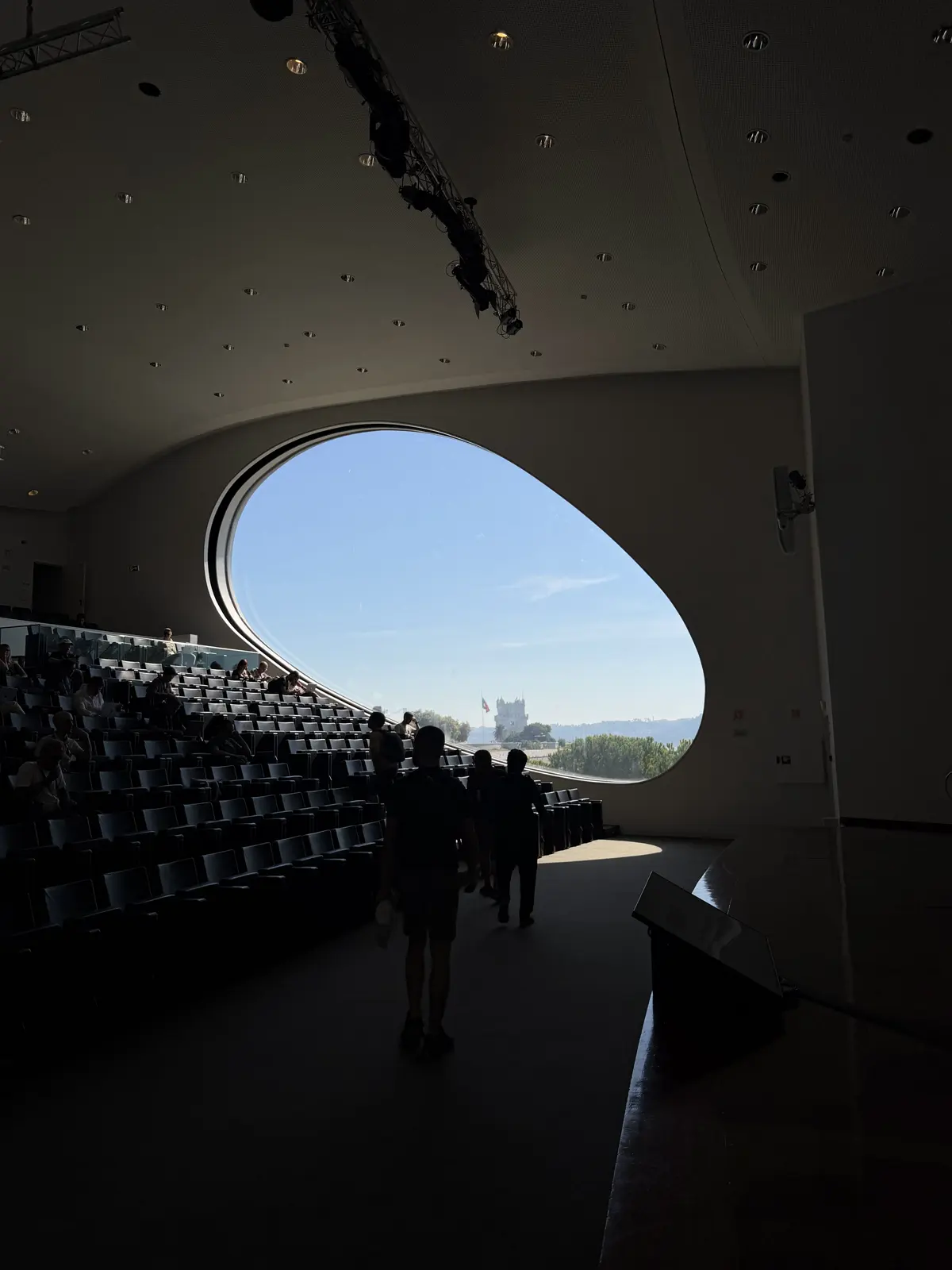 Dark, empty auditorium, with light coming through the oval window and the silhouette of a person walking down the stairs.