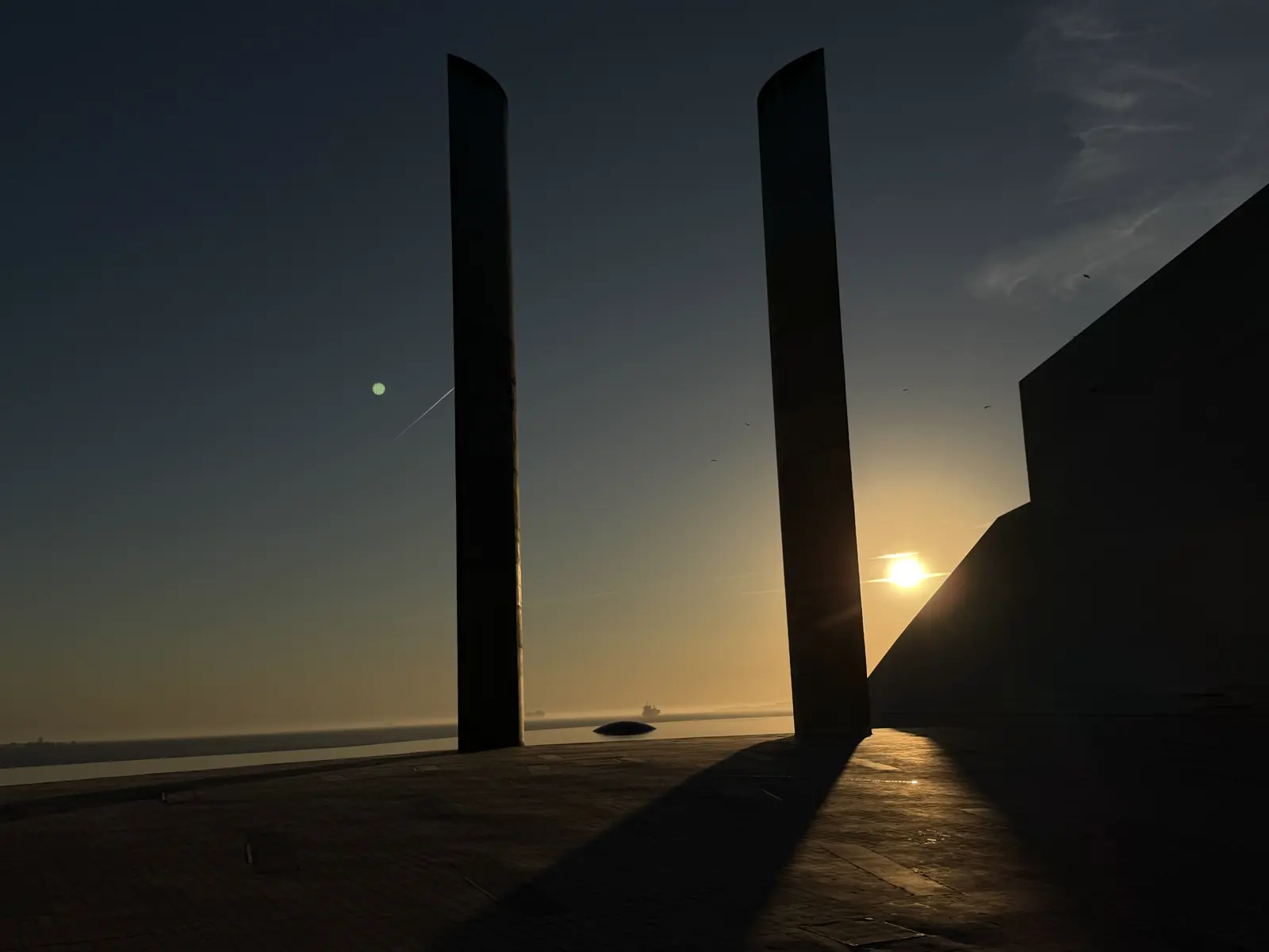 Two tall monoliths in silhouette against the sun setting over the river.